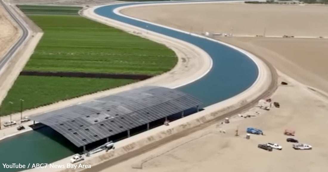 Aerial view of a curved irrigation canal near green fields and a solar-covered structure.
