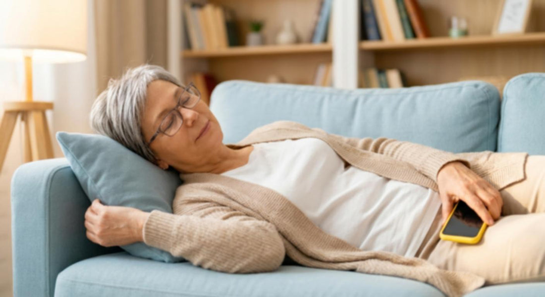 An older woman resting comfortably on a couch, holding a smartphone.