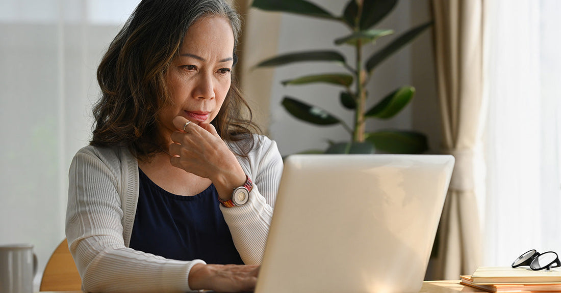 older woman sitting at a desk looking at computer near window