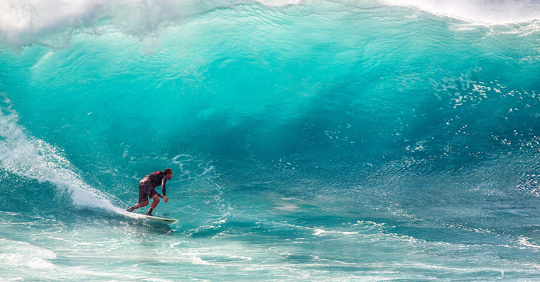 Hands gripping a surfboard with ocean waves in the background.
