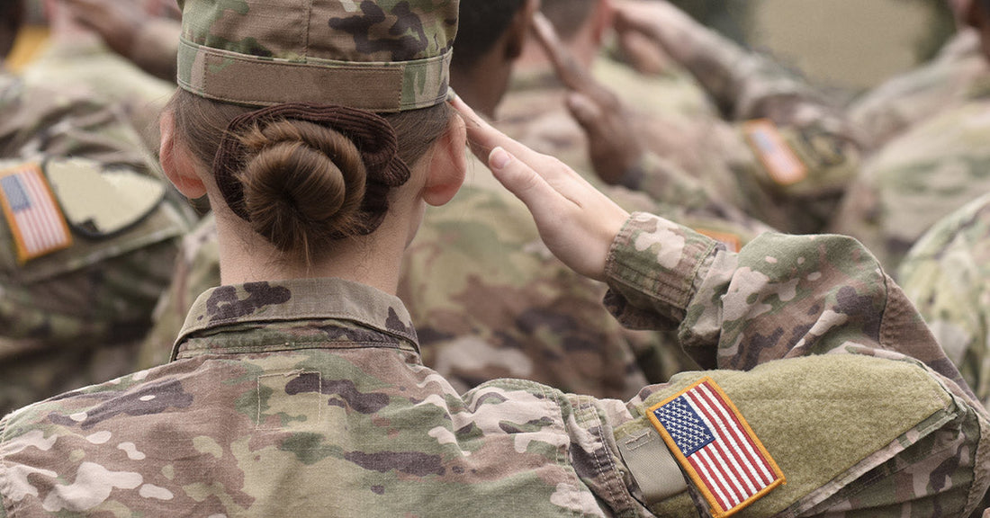 A group of U.S. soldiers in uniform salute, viewed from behind with the American flag patch visible.