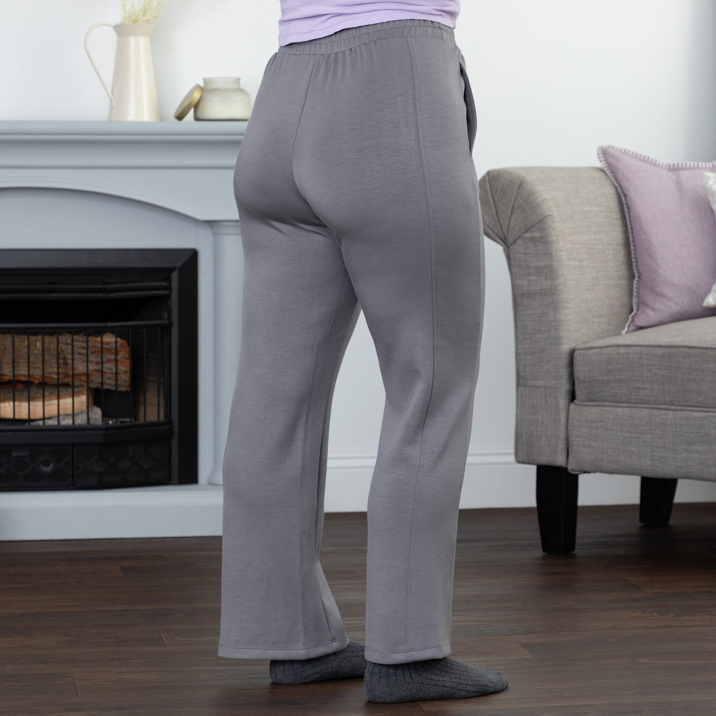 Person wearing gray sweatpants in a living room setting with a fireplace and sofa.