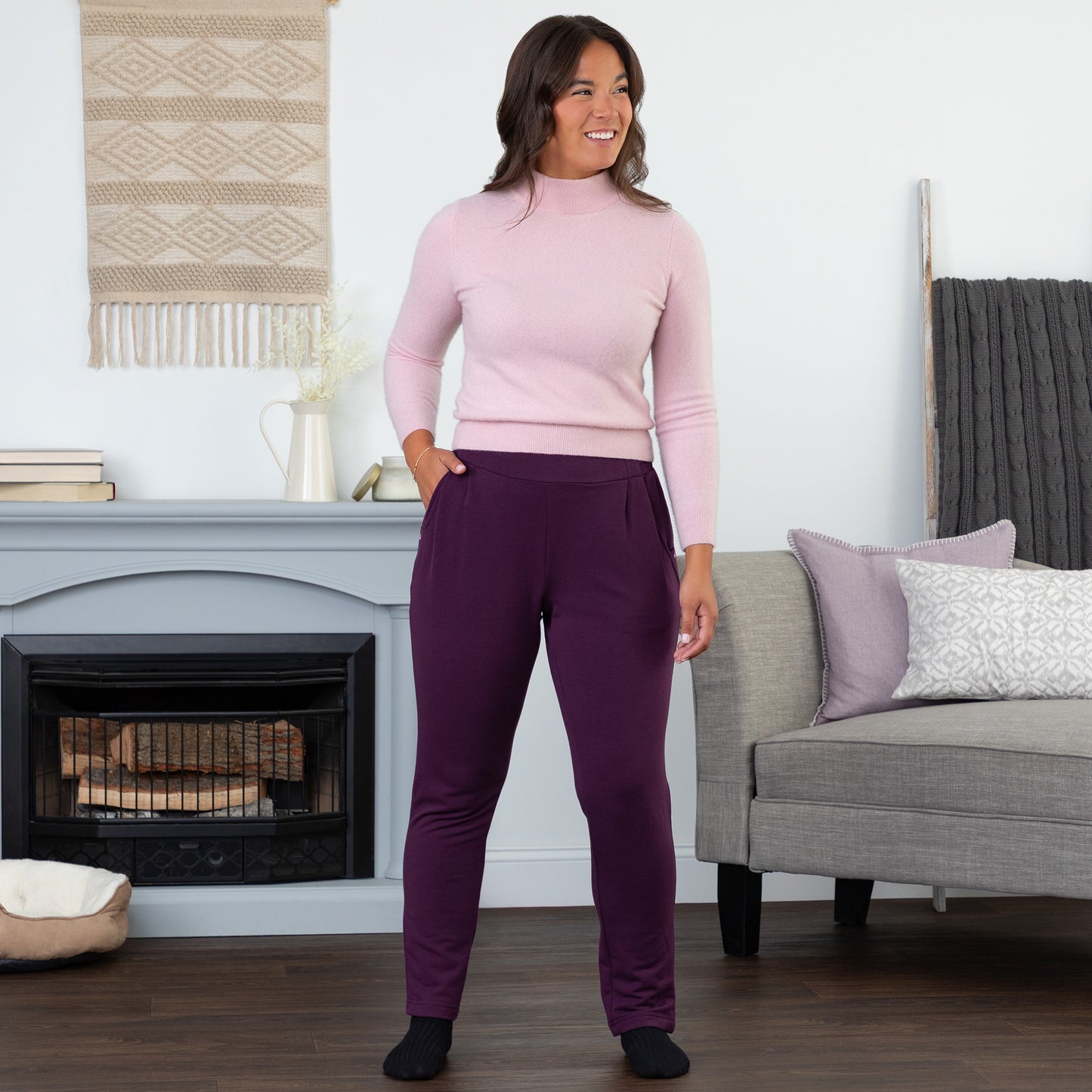 Woman wearing a pink sweater and purple pants standing in a living room.