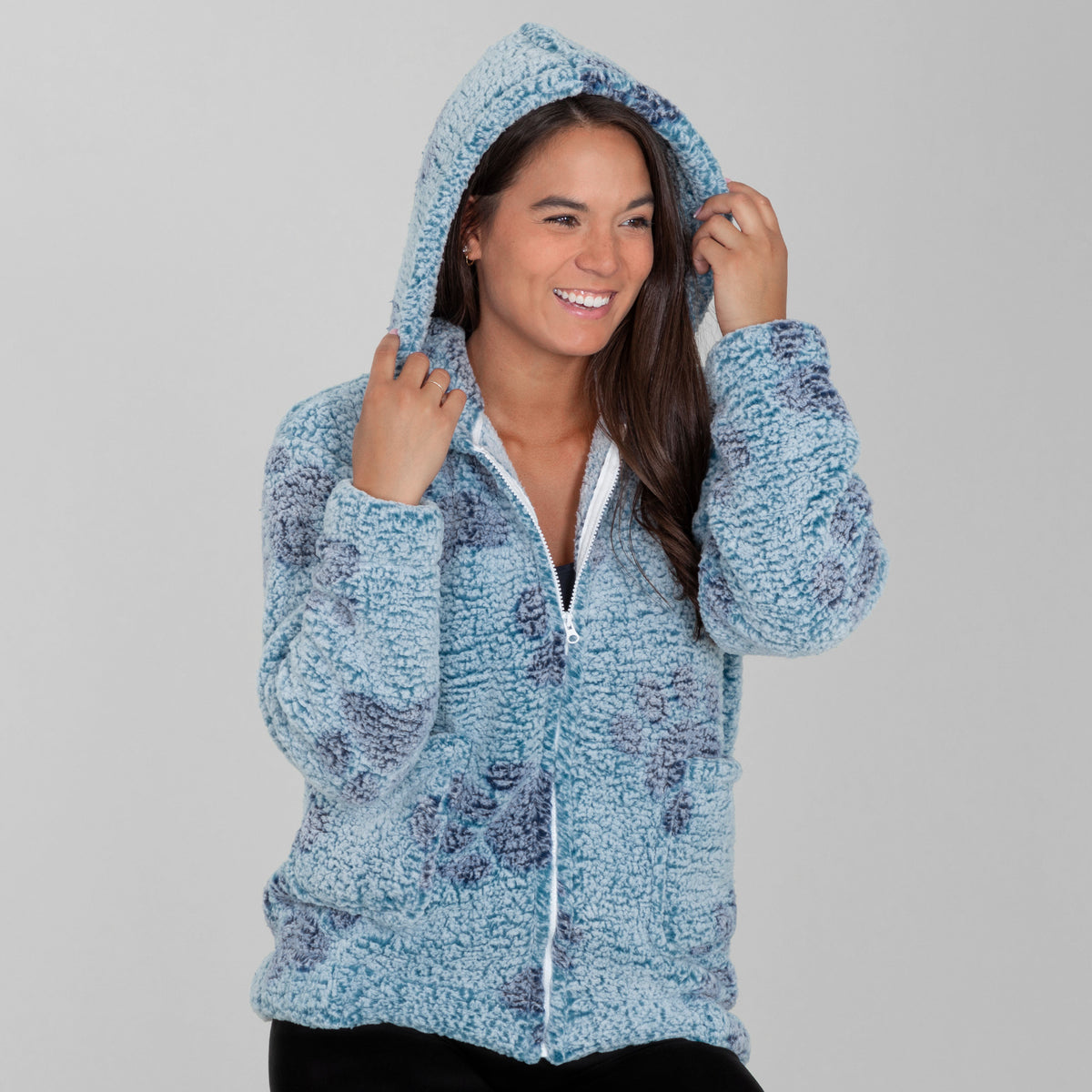 Woman wearing a blue fleece hooded jacket with blue paw prints all over, with two front pockets, against a beige background.