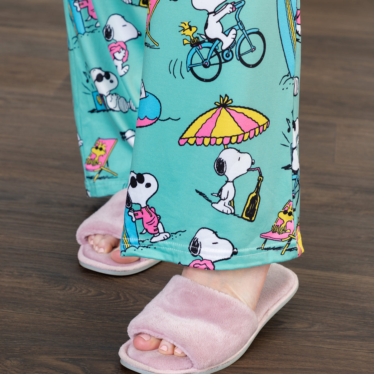 A person standing in a living room wearing lounge pants with a beach pattern and Snoopy-themed prints.