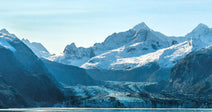 A humpback whale breaches the turquoise waters of a glacial fjord surrounded by snow-capped mountains.