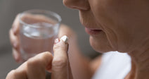woman taking a white pill with glass of water in her hand