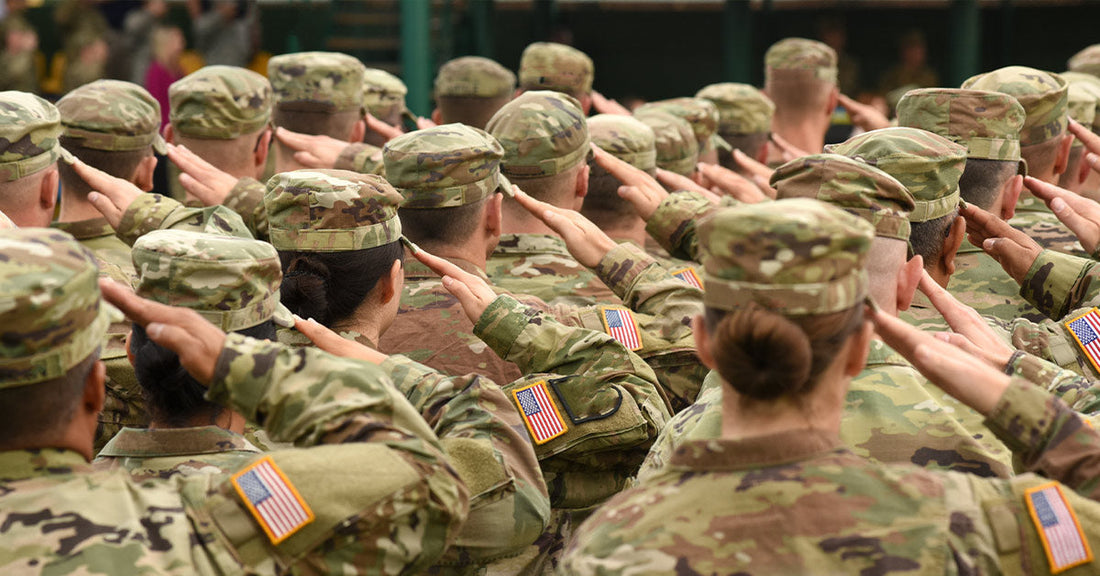 Large group of U.S. service members in camouflage uniforms salute during a formal ceremony.