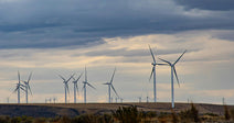 Wind turbines stand against a cloudy sky on a grassy landscape.