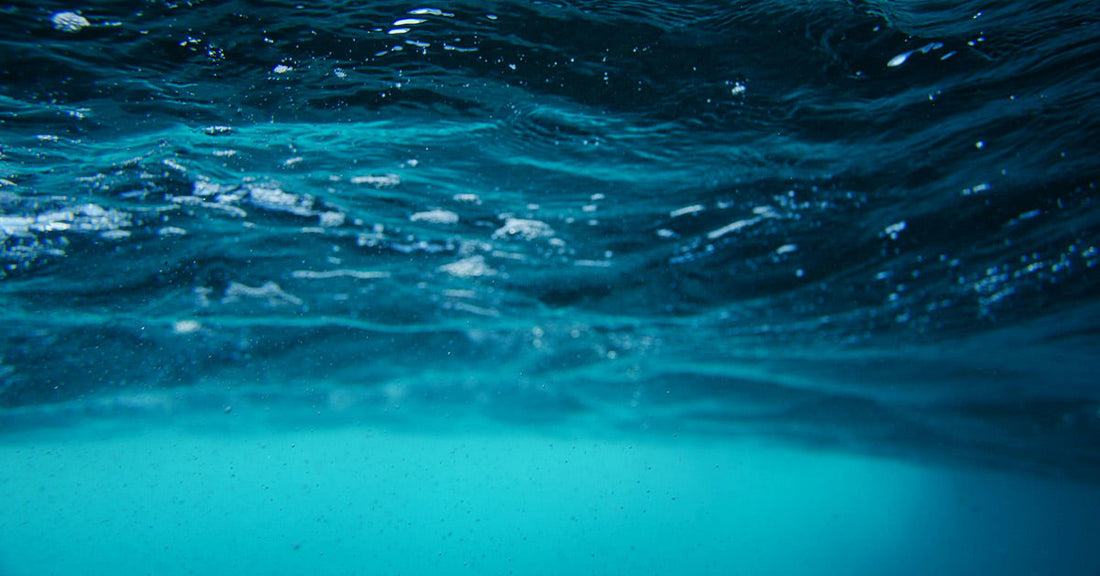 Rippling ocean surface viewed from beneath the water, with light filtering through and shades of deep blue.