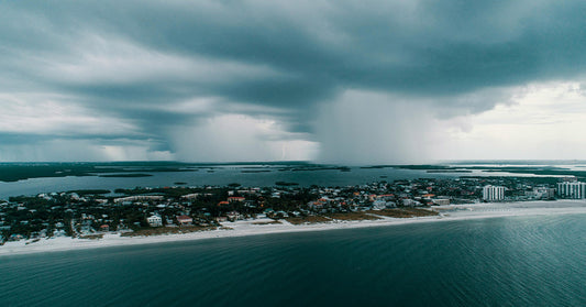 Panoramic aerial image of a coastal city facing a powerful storm, with dark rain clouds and lightning striking offshore.