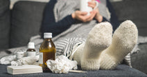sick person with blanket on holding mug on a couch