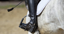 Close-up of a rider's boot in a stirrup on a gray horse.