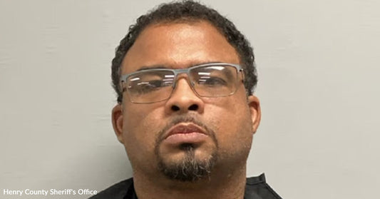 Mugshot of a man wearing glasses against a plain wall background.