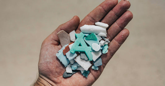 A hand holding a collection of small plastic fragments and debris, including an aqua-colored letter “A.”