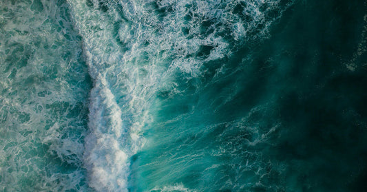 Overhead view of deep blue-green ocean waves mixing with foamy white water in dynamic patterns.