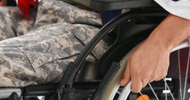 Close-up of a veteran seated in a wheelchair, one hand on the wheel, with an American flag draped across their lap.