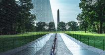 Long view along the Vietnam Veterans Memorial wall with the Washington Monument visible in the distance across the lawn.