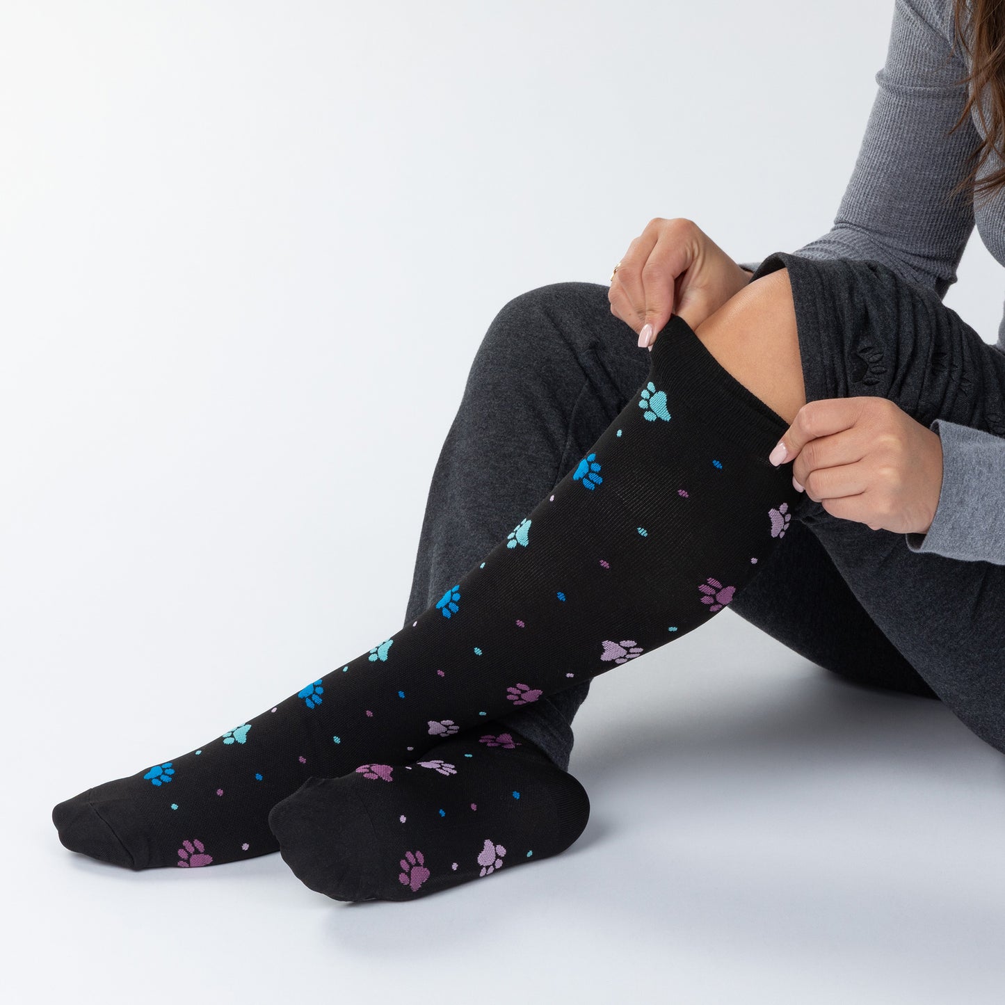 Person wearing black knee-high compression socks with colorful paw prints on a light gray background