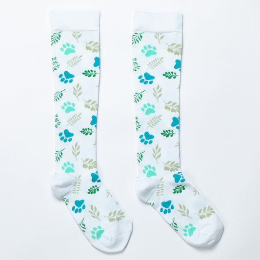 White compression socks with blue and turquoise paw prints and green leafy sprigs.