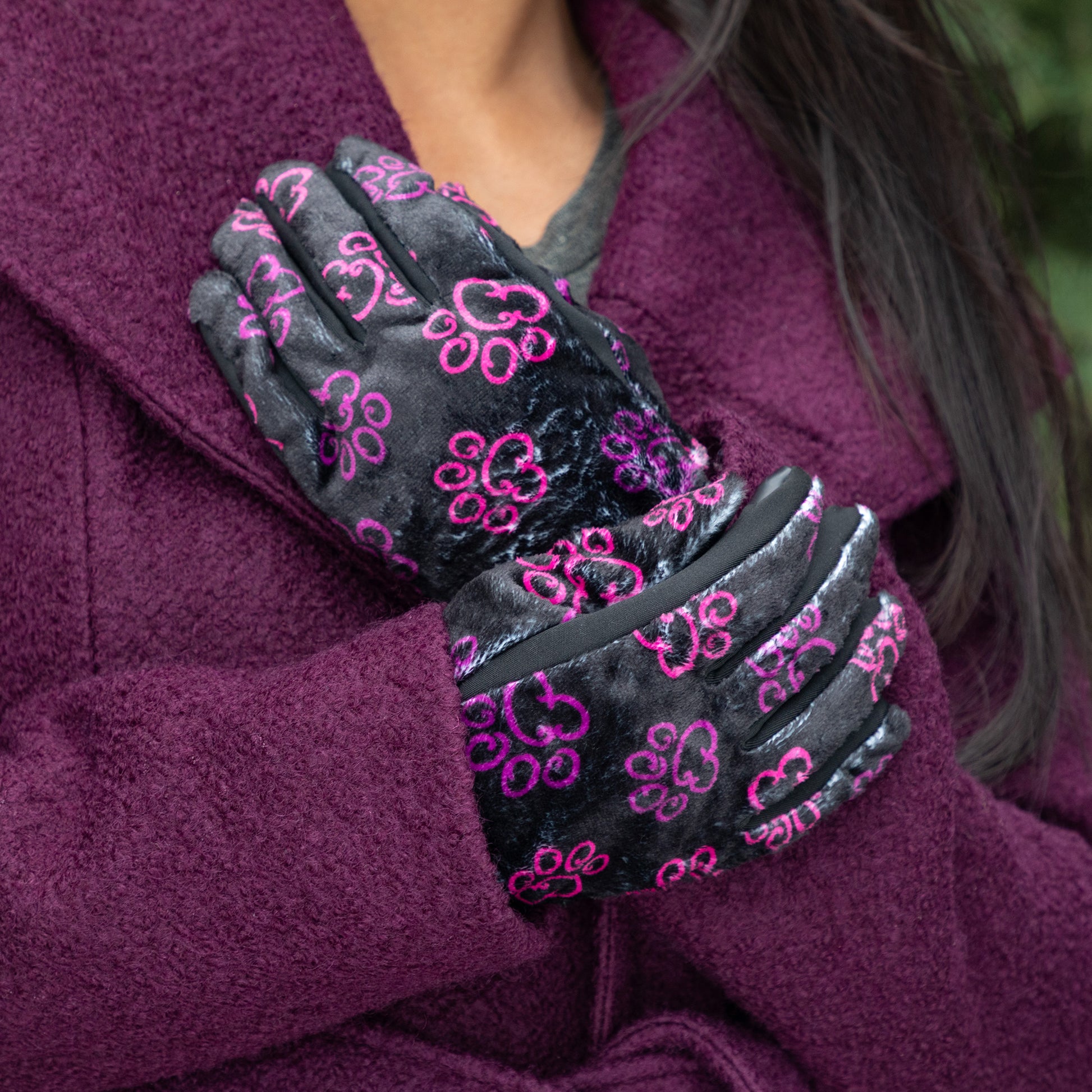 A woman, outside, wearing a coat and a pair of touchscreen technology fingertips warm black fleece gloves adorned with prink and violet elegant paw prints. 