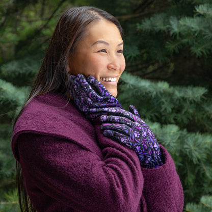 A woman, outside, wearing a coat and a pair of touchscreen technology fingertips warm black fleece gloves adorned with purple paw prints and swirls. 