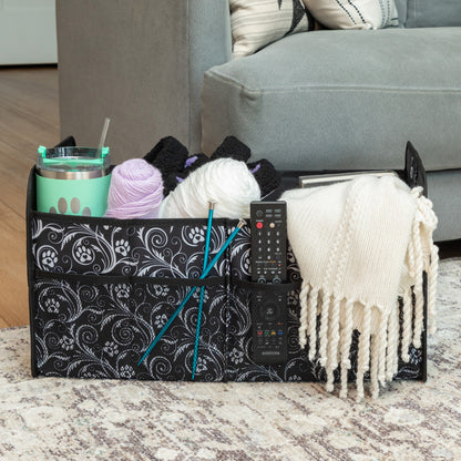 Multifunctional storage caddy with remote control, yarn, and cups on a coffee table.