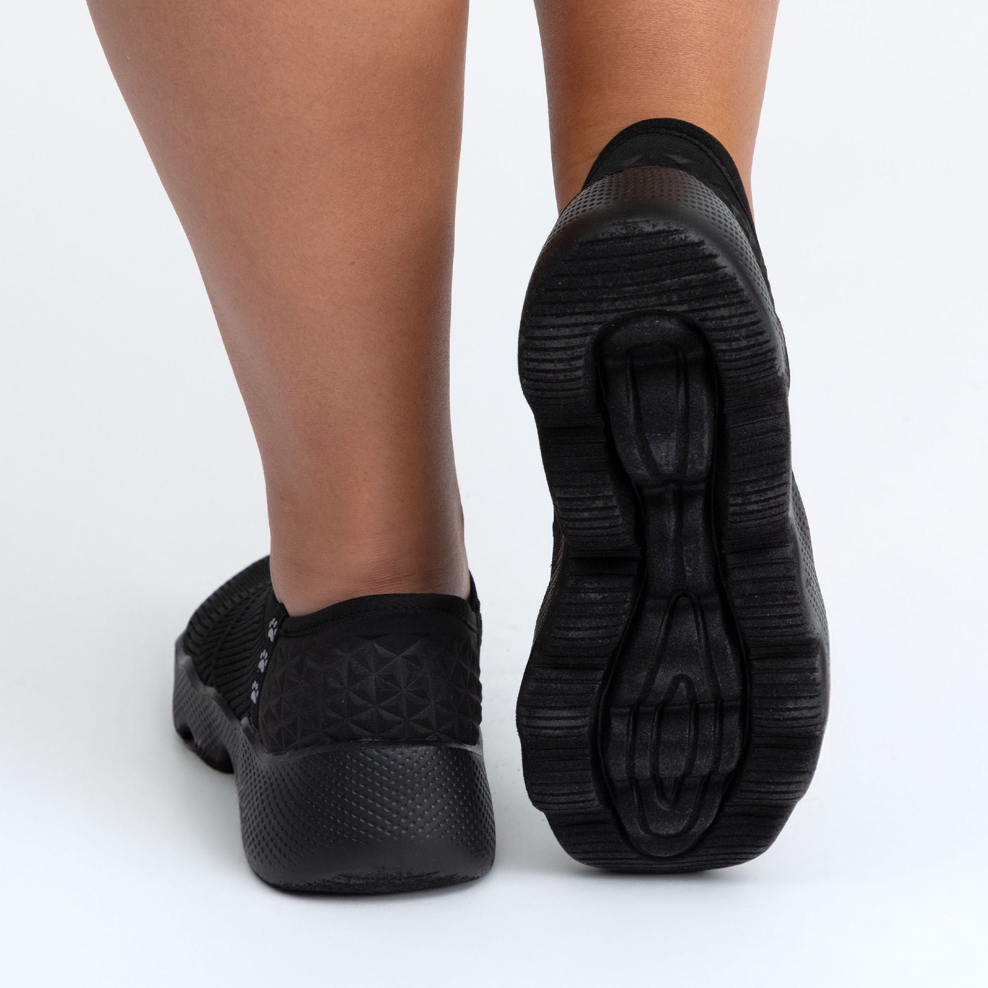 Black slip-on shoes with textured sole on a white background