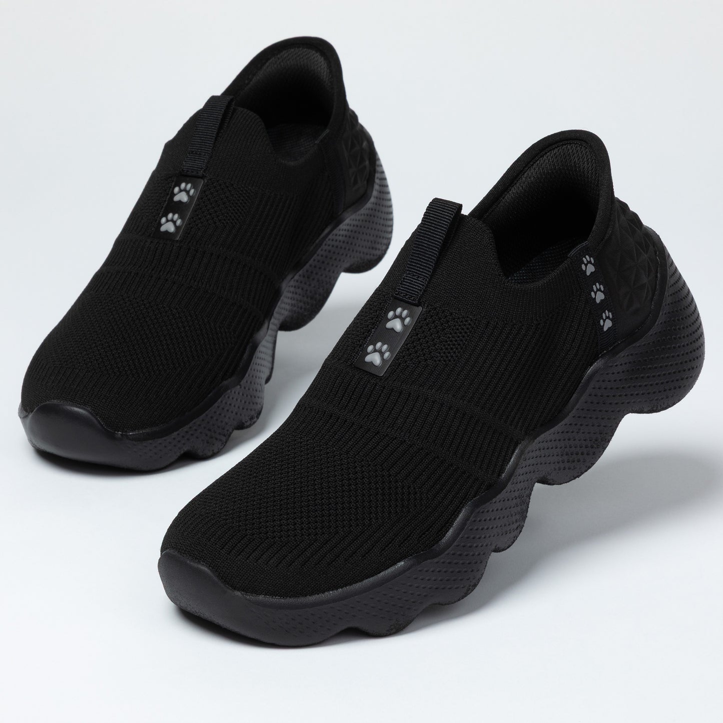 Pair of black slip-on shoes with paw print accents on a light gray background