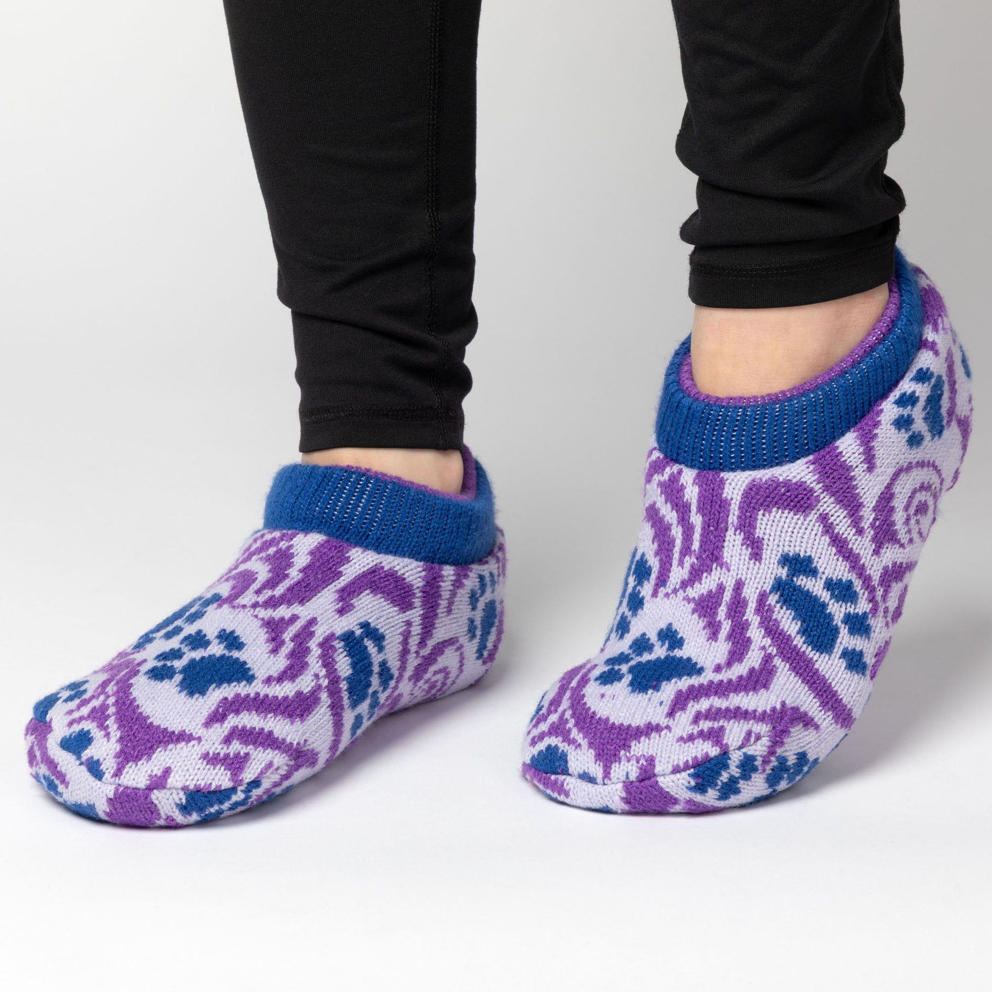 Purple and blue paw print patterned knitted slipper socks worn with black leggings on a light gray background, Paw Symphony