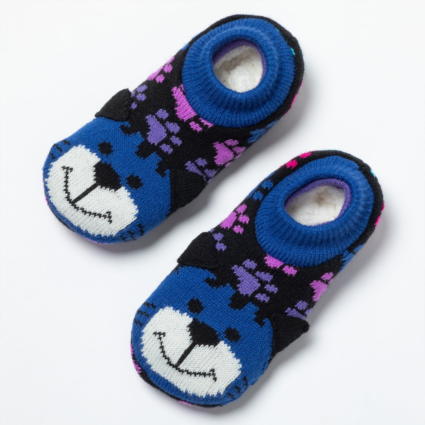 A pair of knit slippers with a blue and black cat face pattern, purple accents, and a white fuzzy lining, shown on a light gray background.