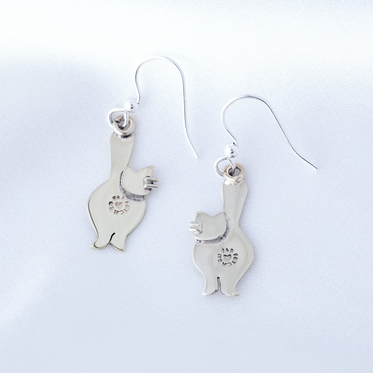 The back of silver cat-shaped earrings on a light gray background
