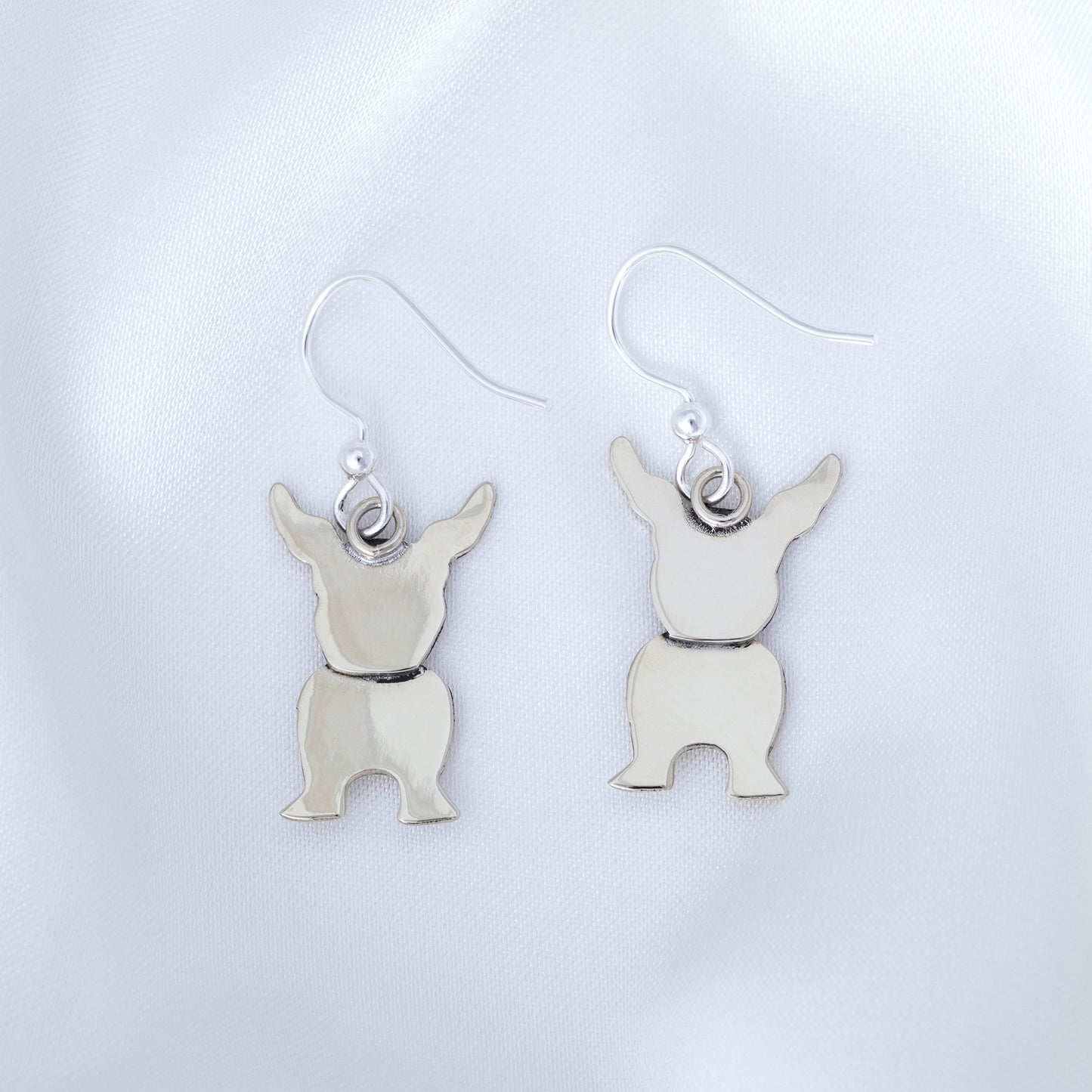 Silver dog-shaped earrings on a light gray background