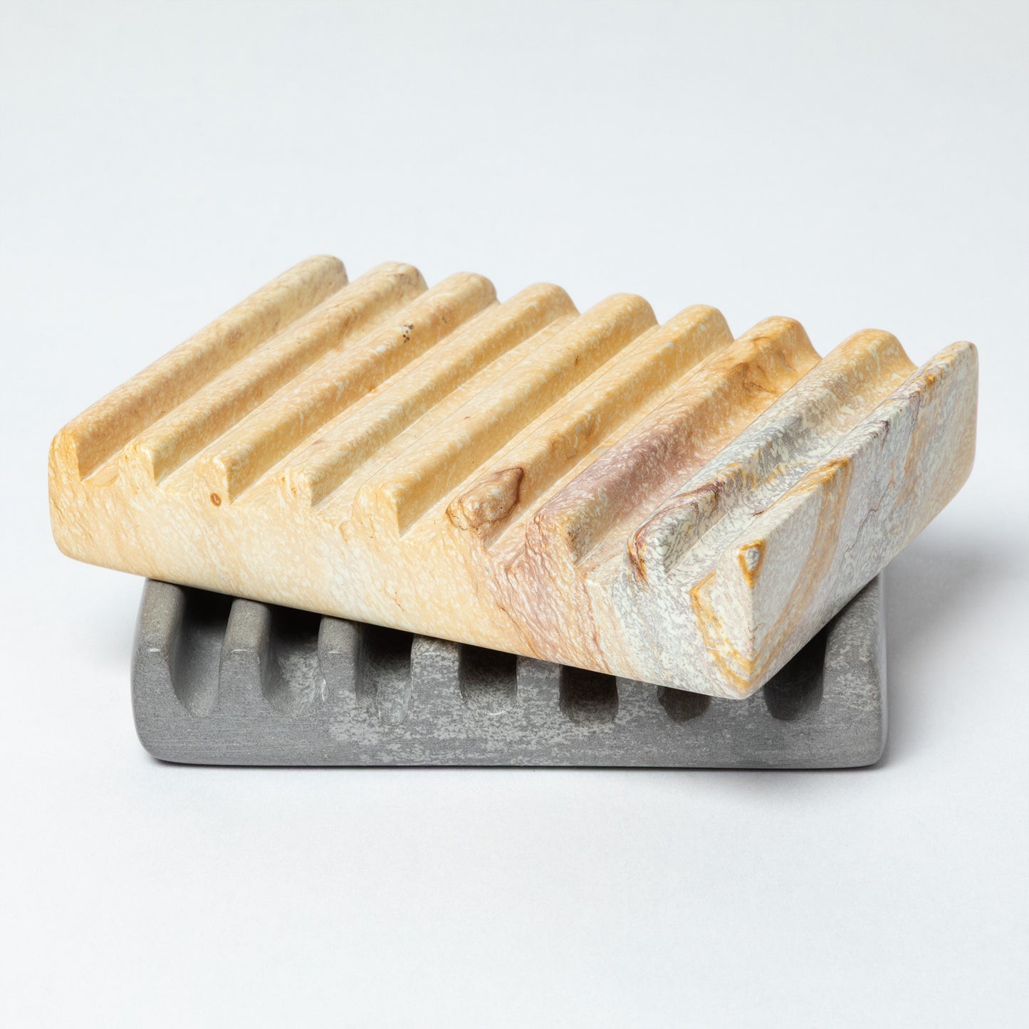 Two soapstone soap dishes, one yellow and one gray, against a white background