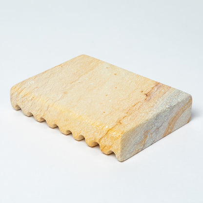 The bottom of a yellow soapstone soap dish, against a white background.