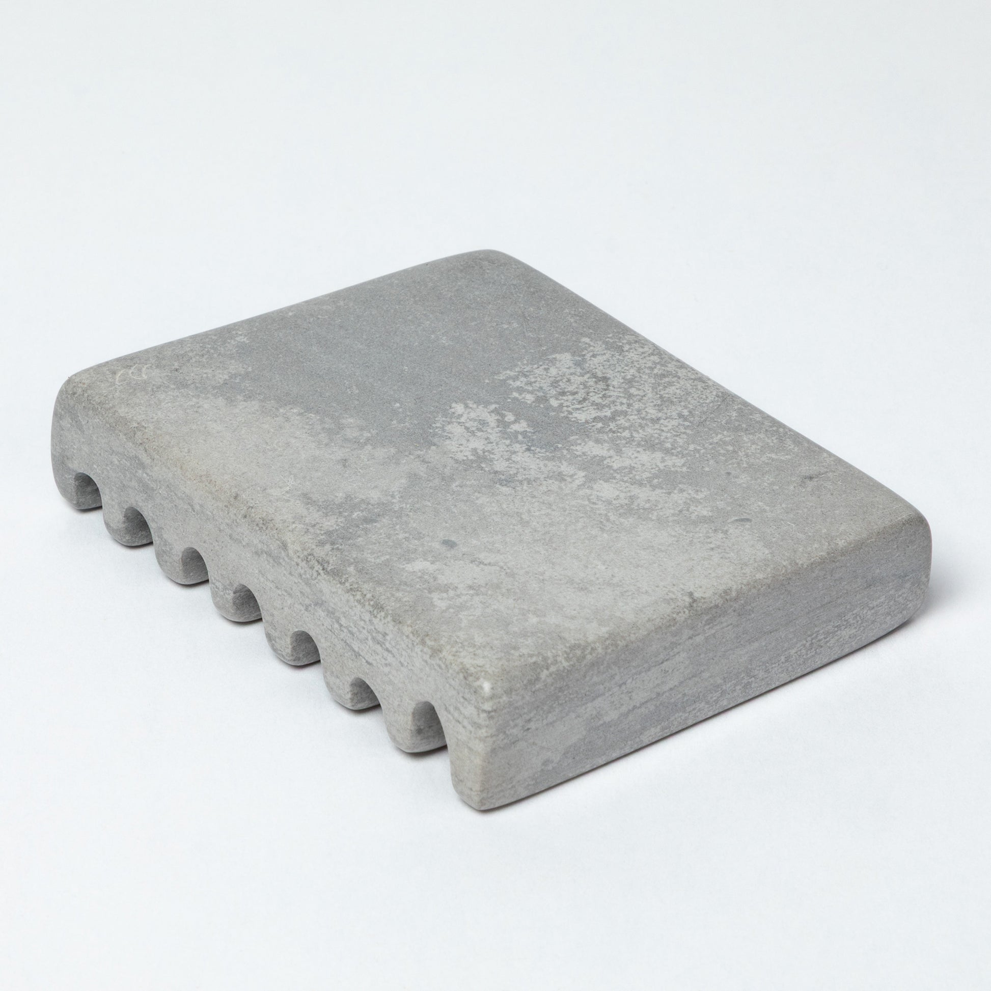 The bottom of a gray soapstone soap dish, against a white background.