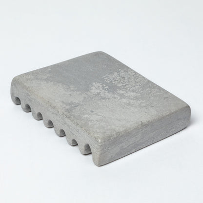 The bottom of a gray soapstone soap dish, against a white background.