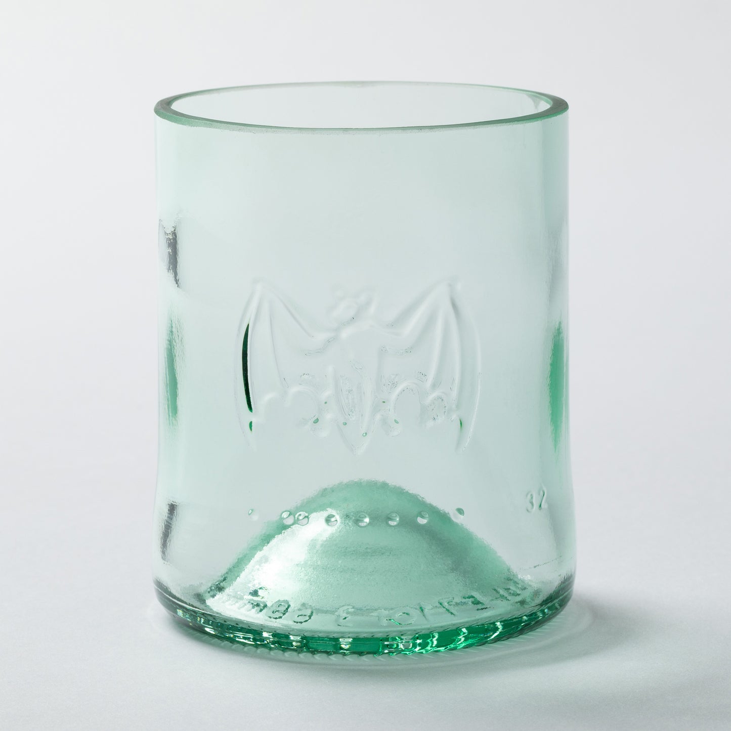 Green glass tumbler made from recycled glass with embossed design on a white background
