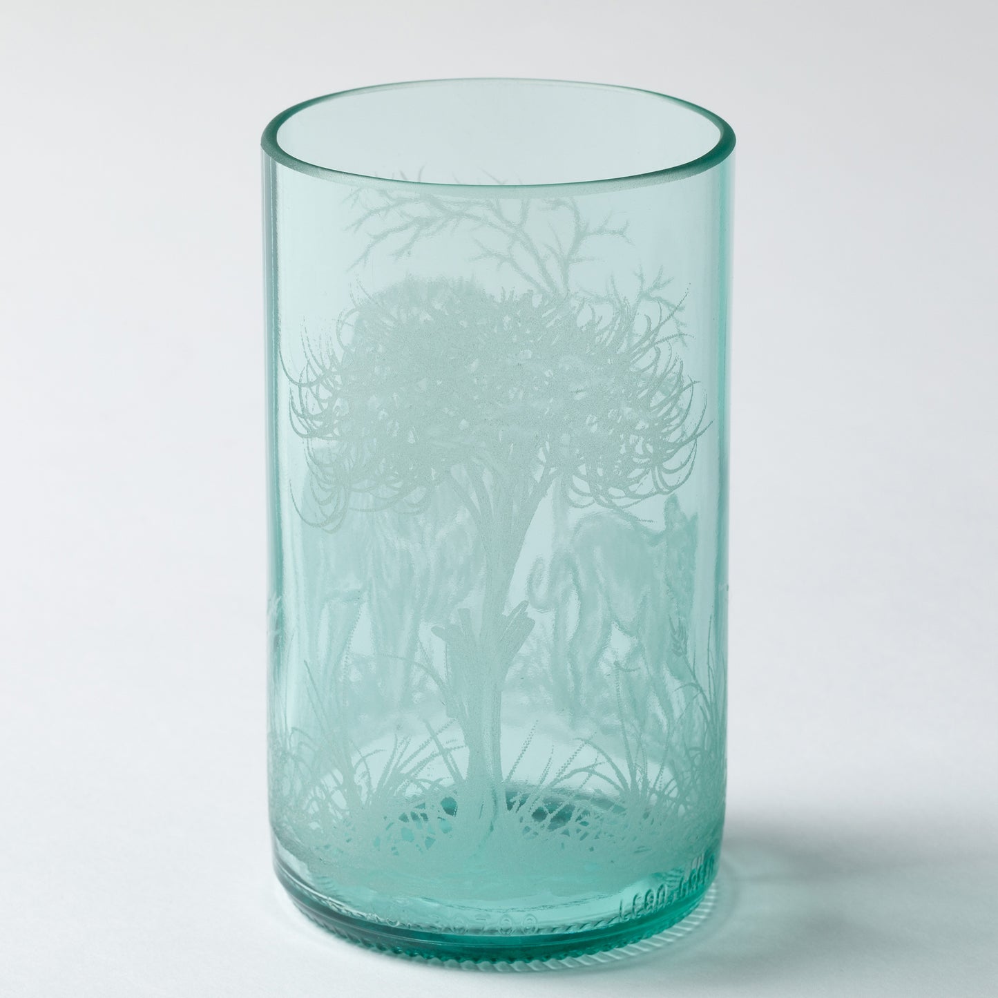 Turquoise glass tumbler with engraved design on a white background