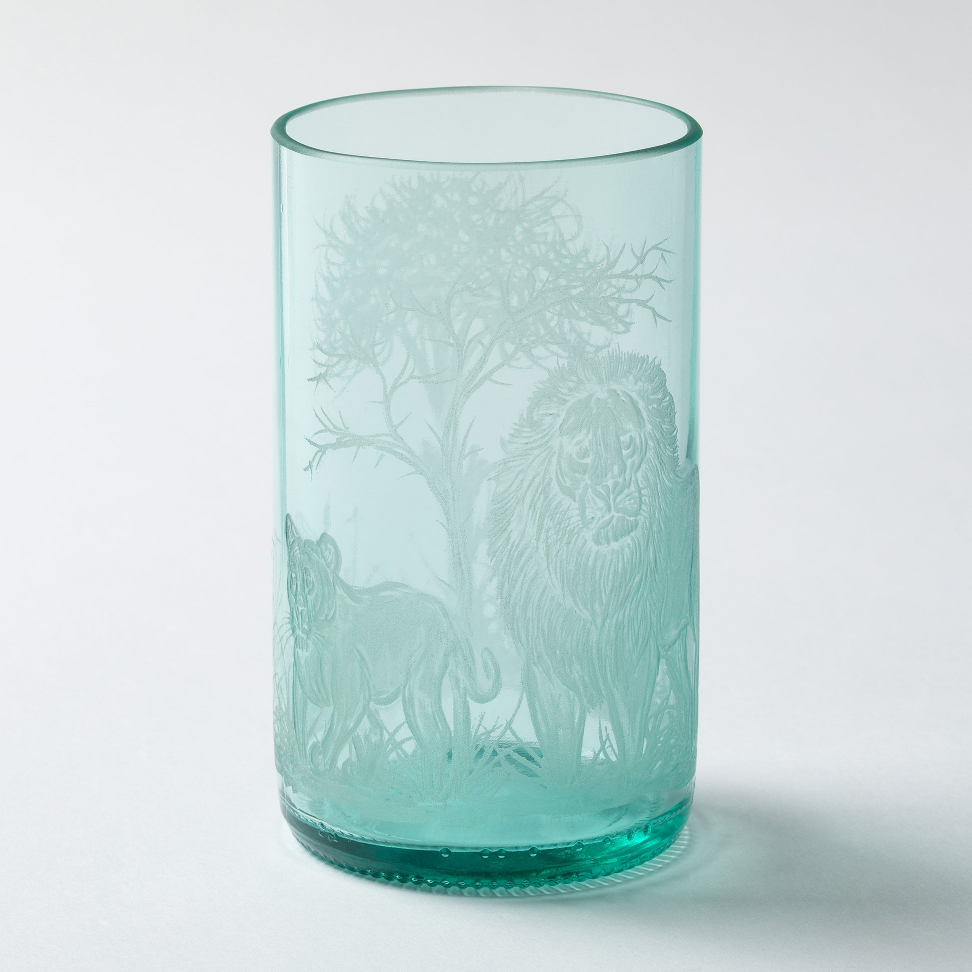 Turquoise glass tumbler with animal etching on a white background