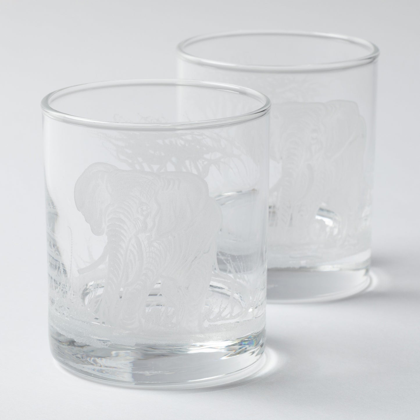 Two clear glass tumblers with engraved designs on a white background