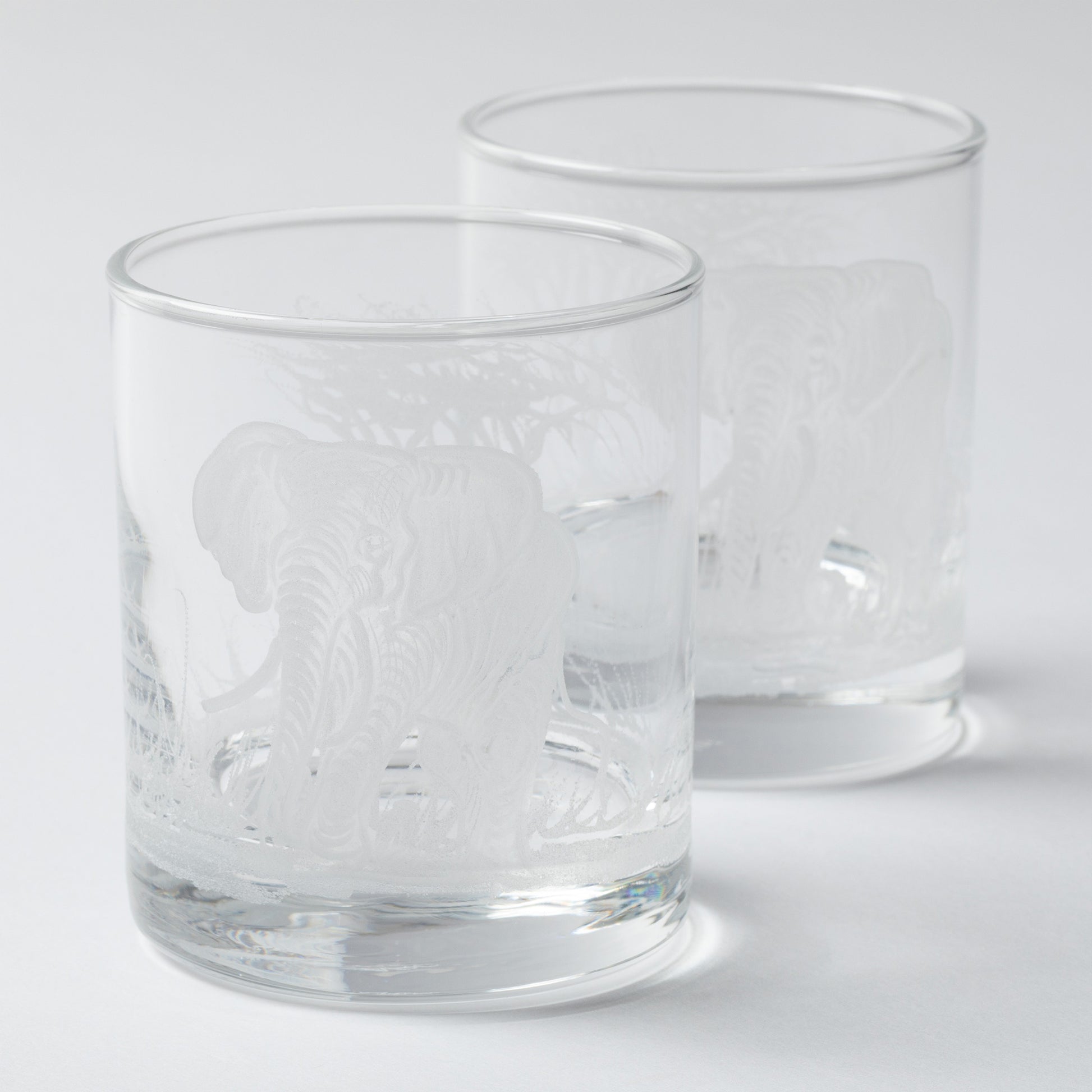 Two clear glass tumblers with engraved designs on a white background