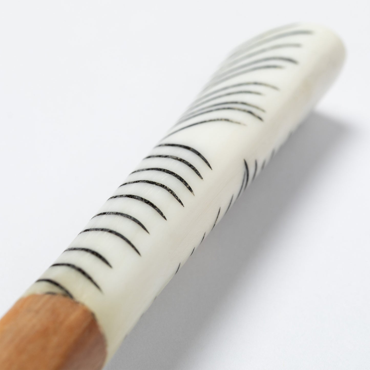 Close-up of a wooden spoon handle with a white bone accent featuring black stripes on a white background.