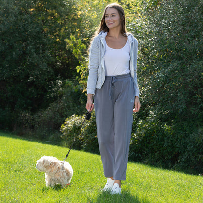 Woman walking a dog in a park with green grass and trees, while wearing gray Paw Print Ultra Soft Modal Pants​.