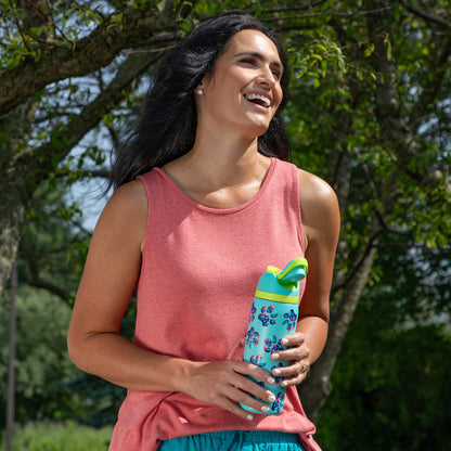 Smiling woman holds a colorful water bottle outdoors, surrounded by greenery.