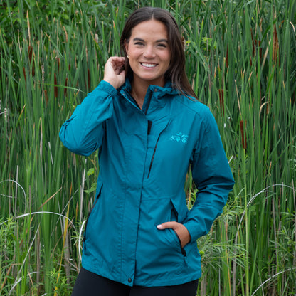 Woman wearing a teal rain jacket standing in tall green grass.