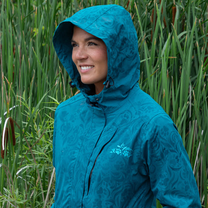 Person wearing a blue raincoat with the hood pulled up, standing in tall green grass.