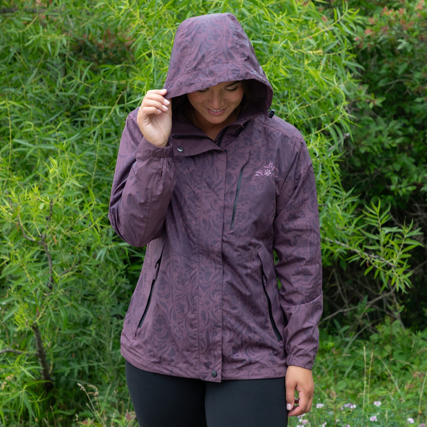 Person wearing a purple raincoat with a paw print swirling pattern in a natural setting with greenery.