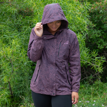 Person wearing a purple raincoat with a paw print swirling pattern in a natural setting with greenery.