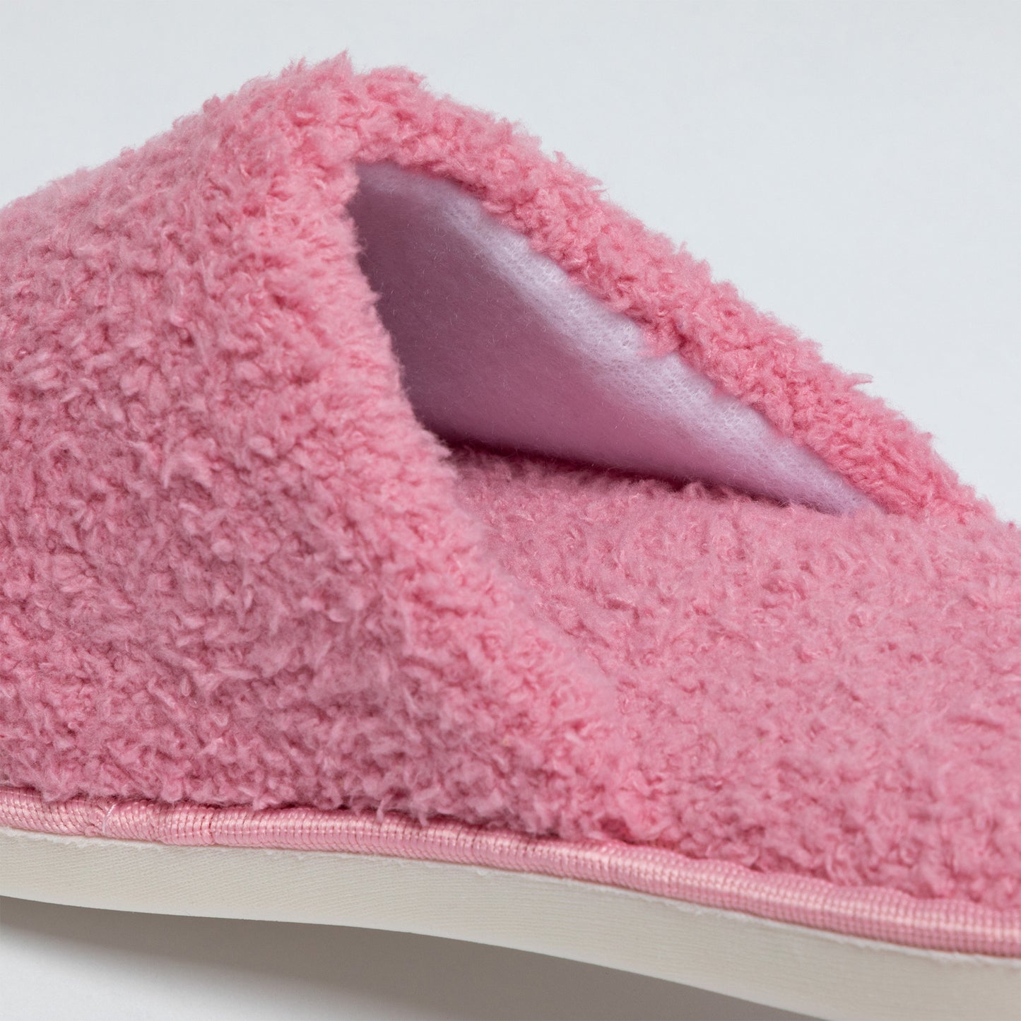 Close-up of a pink fuzzy slipper with a white sole on a light gray background